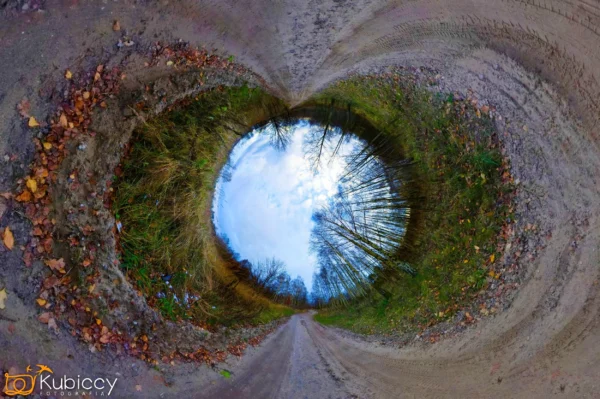 Okrągłe zdjęcie z obiektywem typu rybie oko przedstawiające polną ścieżkę otoczoną drzewami i opadłymi liśćmi, z błękitnym niebem w centrum, tworzącym efekt tunelu lub "małej planety". Logo Kubiccy Photography pojawia się w lewym dolnym rogu. - Kubiccy Fotografia - Fotograf Łódź