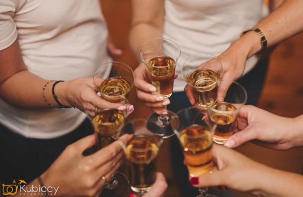 Grupa osób ubranych w białe topy brzęczy kieliszkami wina musującego podczas uroczystego toastu, uchwyconego z góry. - Kubiccy Fotografia - Fotograf Łódź